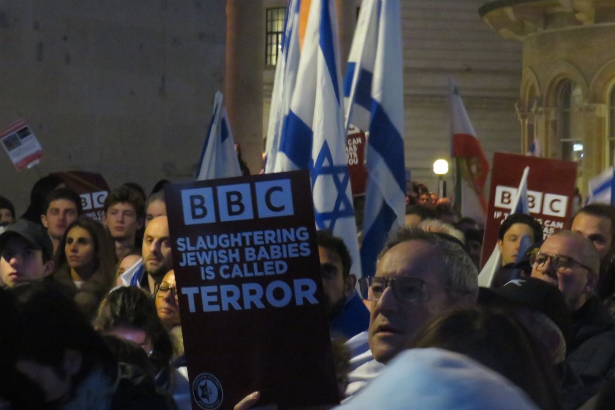תמונה של הפגנה עם דגלי ישראל ושלט עליו נכתב באנגלית: "BBC, לשחוט ילדים יהודים נקרא 'טרור'"