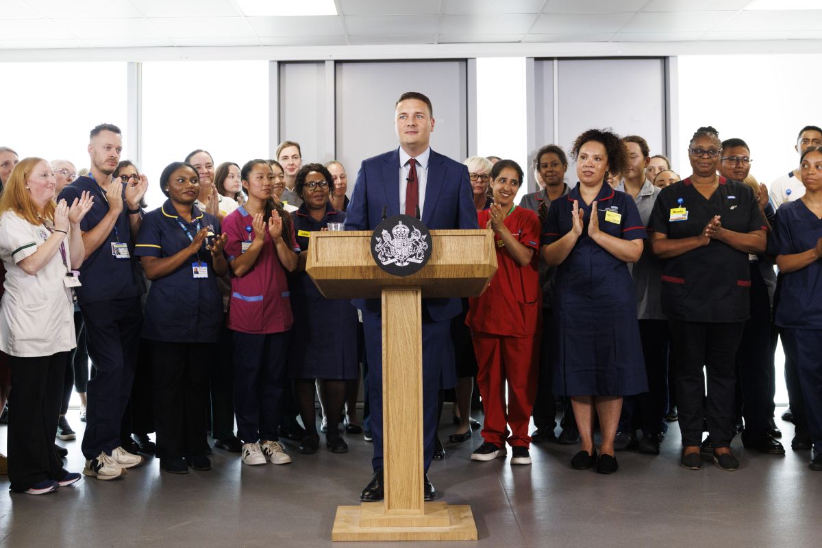 תמונה של שר הבריאות הבריטי וס סטריטינג נואם כשמאחוריו אנשי רפואה