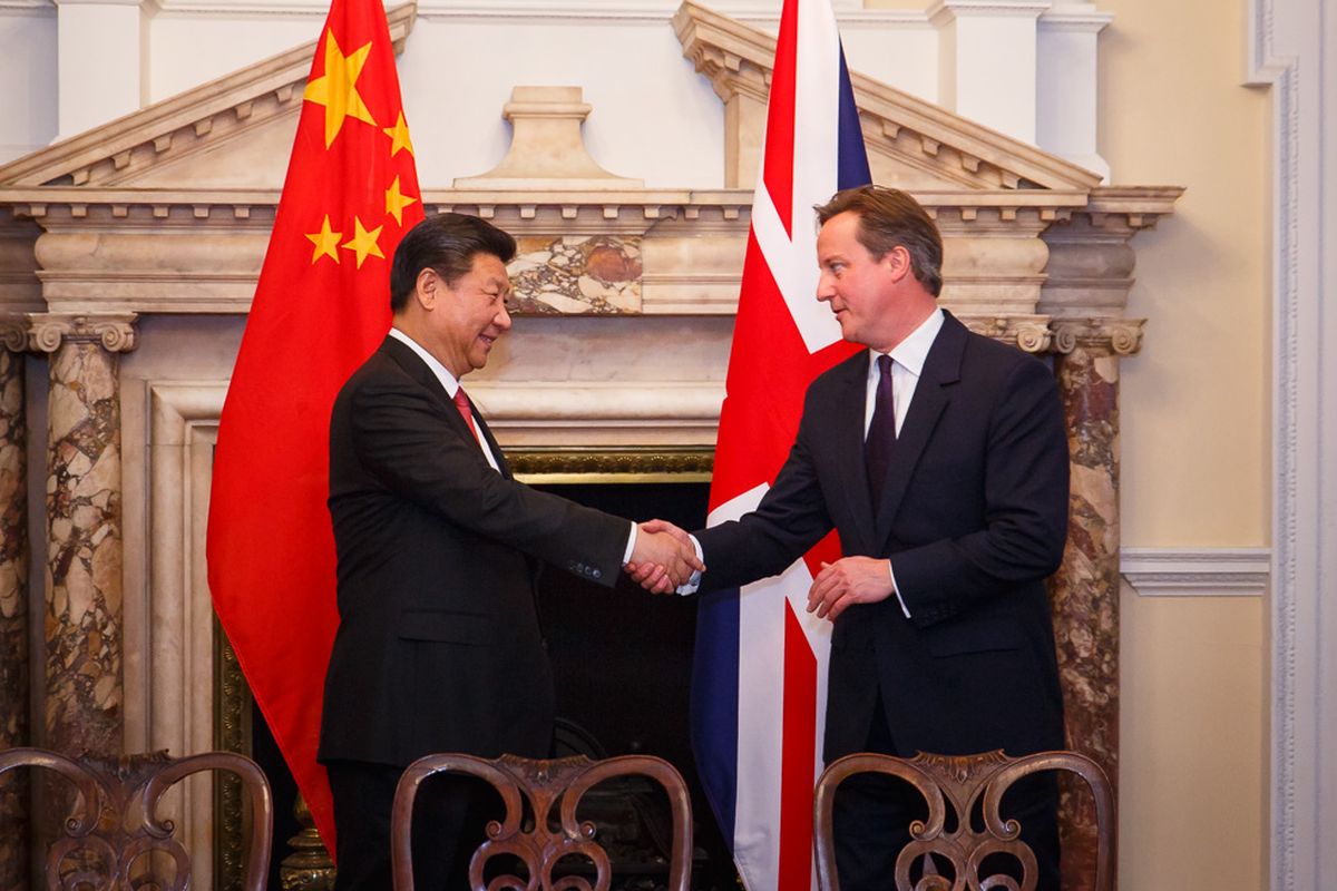דייוויד קמרון ושי ג'ינפינג לוחצים ידיים כשמאחוריהם דגלי בריטניה וסין